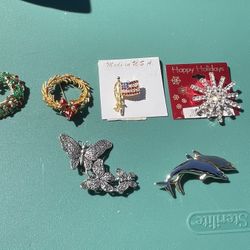 These items are various types of collectible costume jewelry brooch pins, including a holiday wreath, a flag, a festive starburst, filigree butterflie