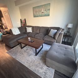 Grey couch, ottoman, coffee table, rug, and TV stand