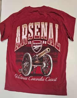 Arsenal F.C. graphic t-shirt featuring a large cannon graphic, the club's "18 | Arsenal | 86" badge details, and the Latin motto "Victoria Concordia C