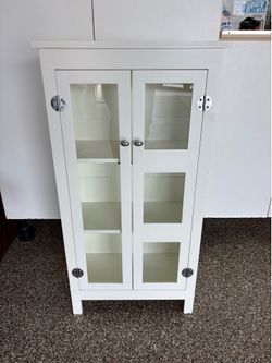 This white freestanding cabinet features two glass-front doors with distinct rectangular panel styles and chrome knobs