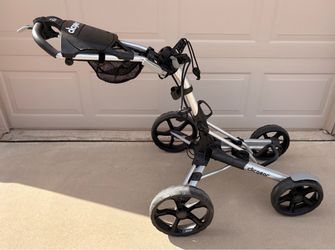 Clicgear Model 8, 4 wheel push golf cart with a silver aluminum frame, four black wheels, ergonomic handle, and a built-in bag holder.