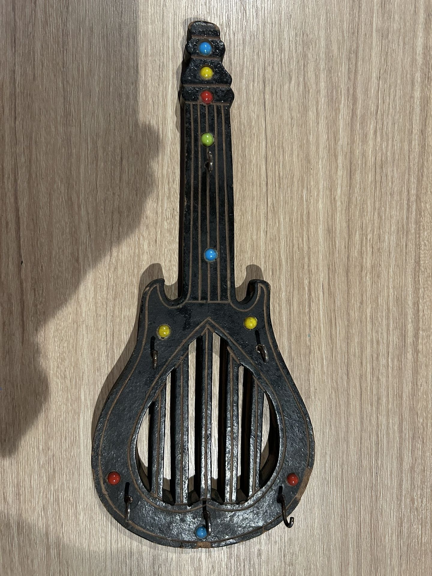 Small wall-mounted decorative guitar with six small hooks and the loop to hang it with