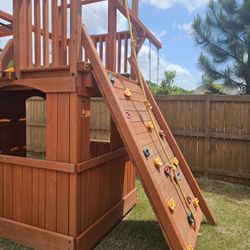 
Woodplay Playhouse 6ft Deck with Bonus Room Playhouse underneath, Rock Climbing Wall, Monkey Bars and an Accessory Arm with a Trapeze Bar.