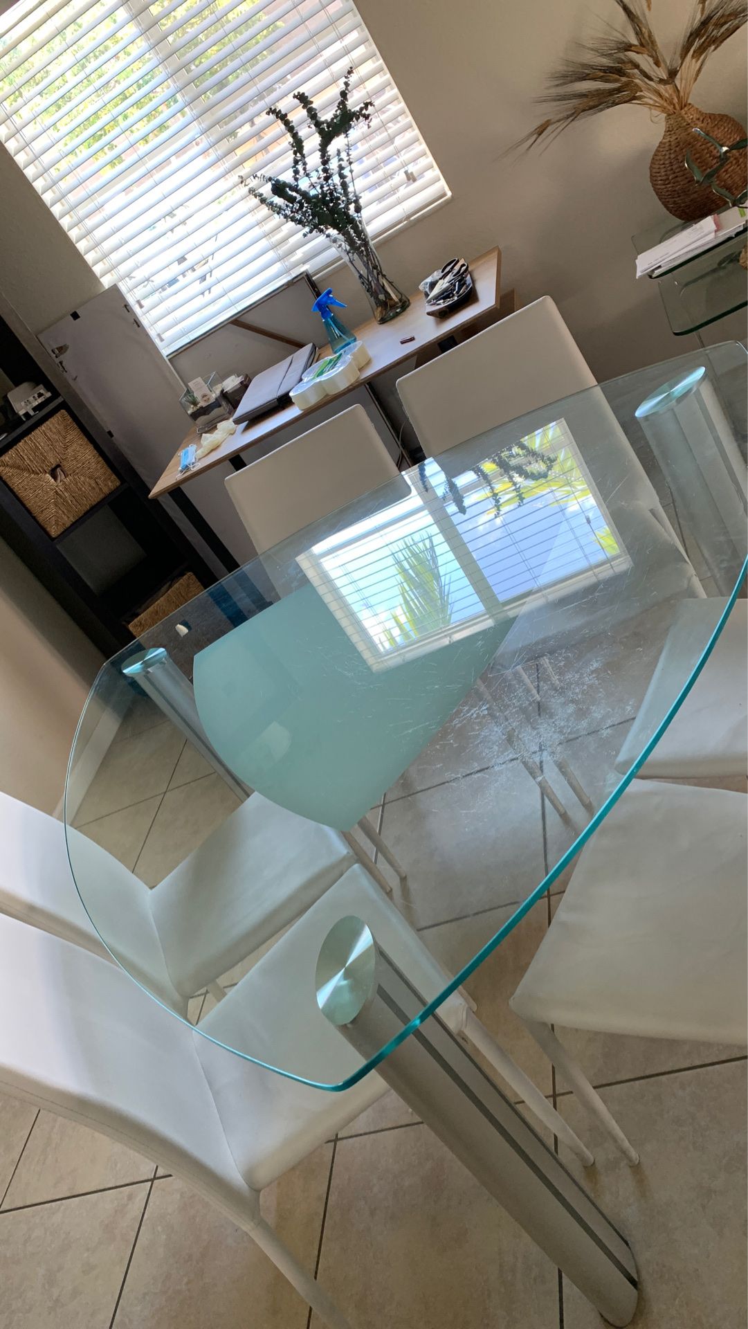 Mesa de comedor en vidrio y acero con seis sillas blancas.