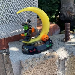 You are bidding on one solar Halloween Witch dressed in black with a green face and hands.  She is riding an orange broom under a yellow moon.  It is 