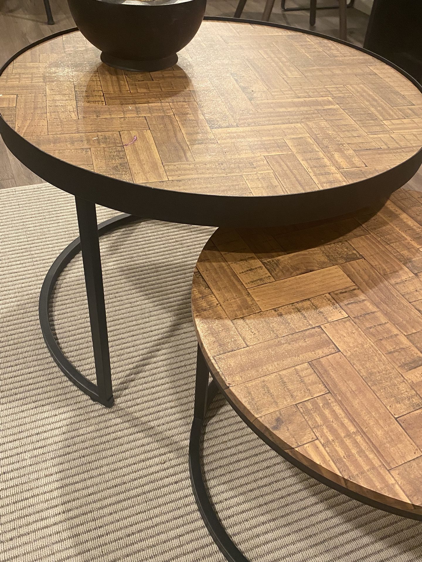 Set Of 2 Nesting Coffee Tables 30” And 24” In Diameter. Matte black Metal Base And Herringbone Wood Top