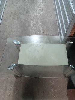 modern glass dining table with four chrome/stainless-steel cylindrical pedestal legs.