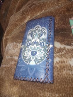 This is a blue vegan leather wallet featuring a Hamsa hand and evil eye design with hand-stitched brown