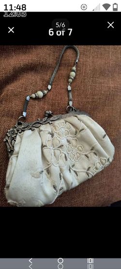 vintage-style ivory fabric evening bag features an ornate, antique-finish metal kiss-lock frame and a beaded top handle.