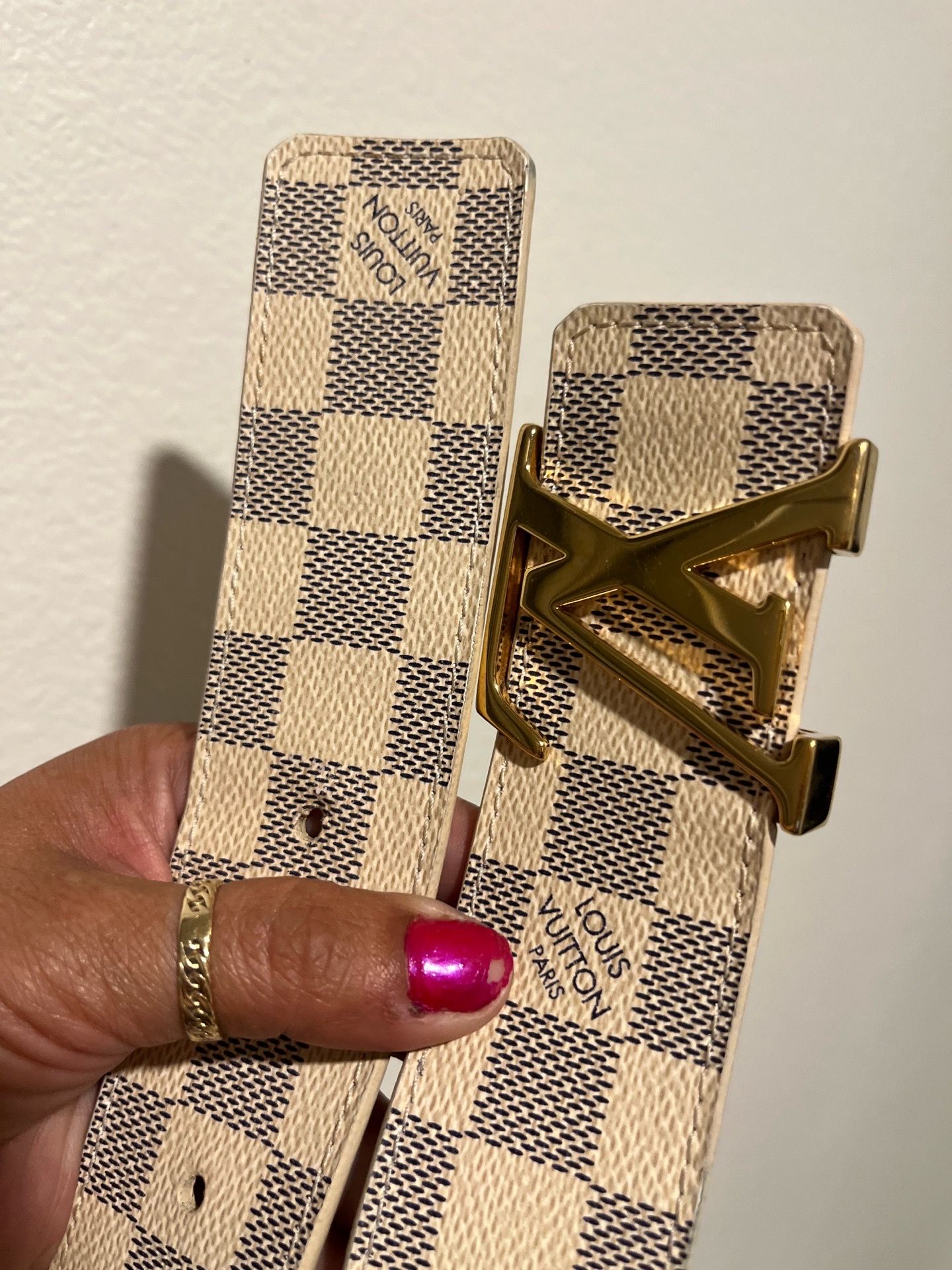 The item pictured is a Louis Vuitton Damier Azur canvas belt featuring a gold-toned LV Initiales buckle.