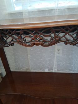 Brown wooden foyer/living room table. Has some carving on the front of the table.