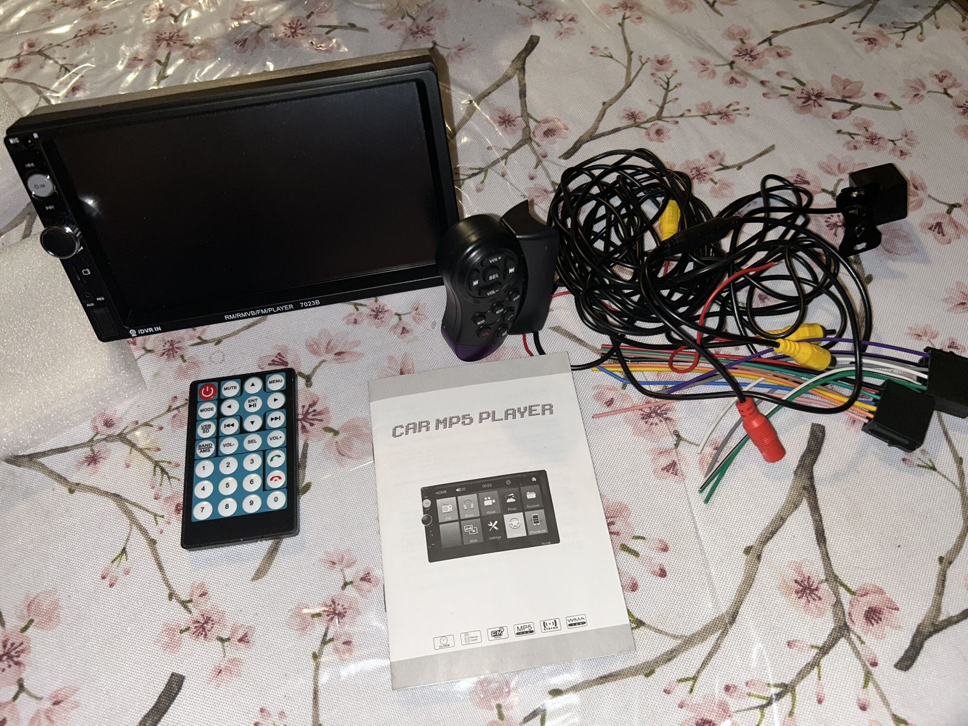 a 7-inch car MP5 player, model 7023B, along with its accessories, including a remote control and wiring harnesses.