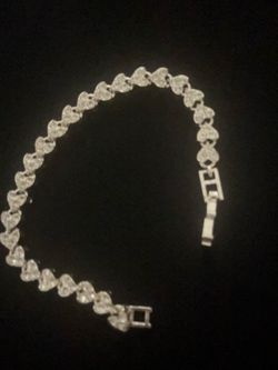 Elegant silver-tone tennis bracelet with heart-shaped links. Each link is set with clear, faceted stones. The piece has a secure fold-over clasp closu