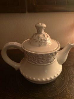 white ceramic teapot with an embossed floral band around the rim