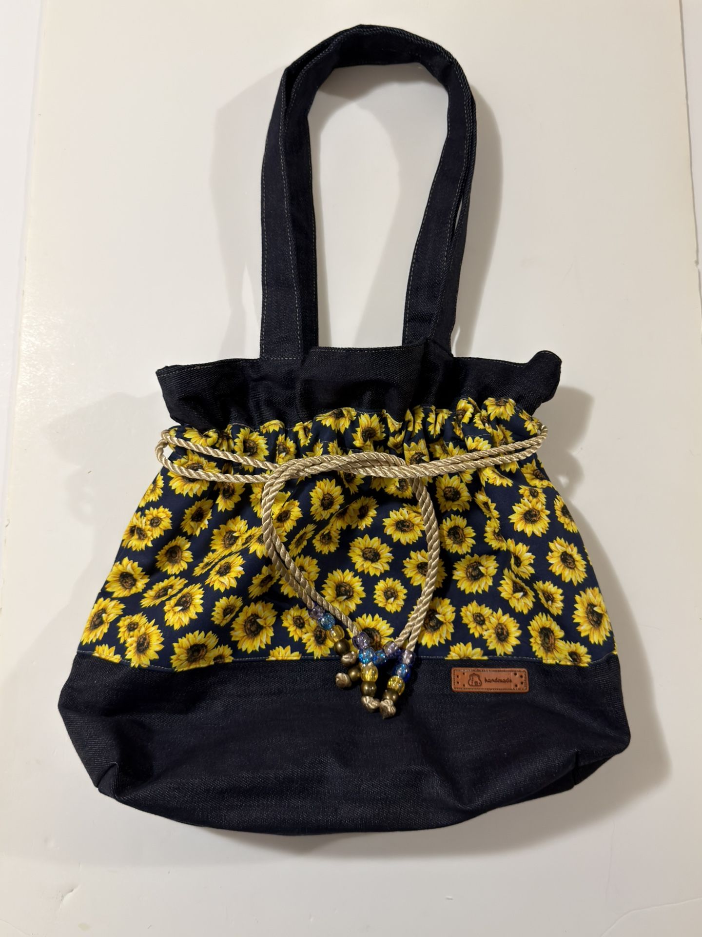 The Denim Midnight With Yellow Sun Flowers Print Medium 16X18 Drawstring Tote Bag is a stylish and versatile accessory for women. Made from a denim an