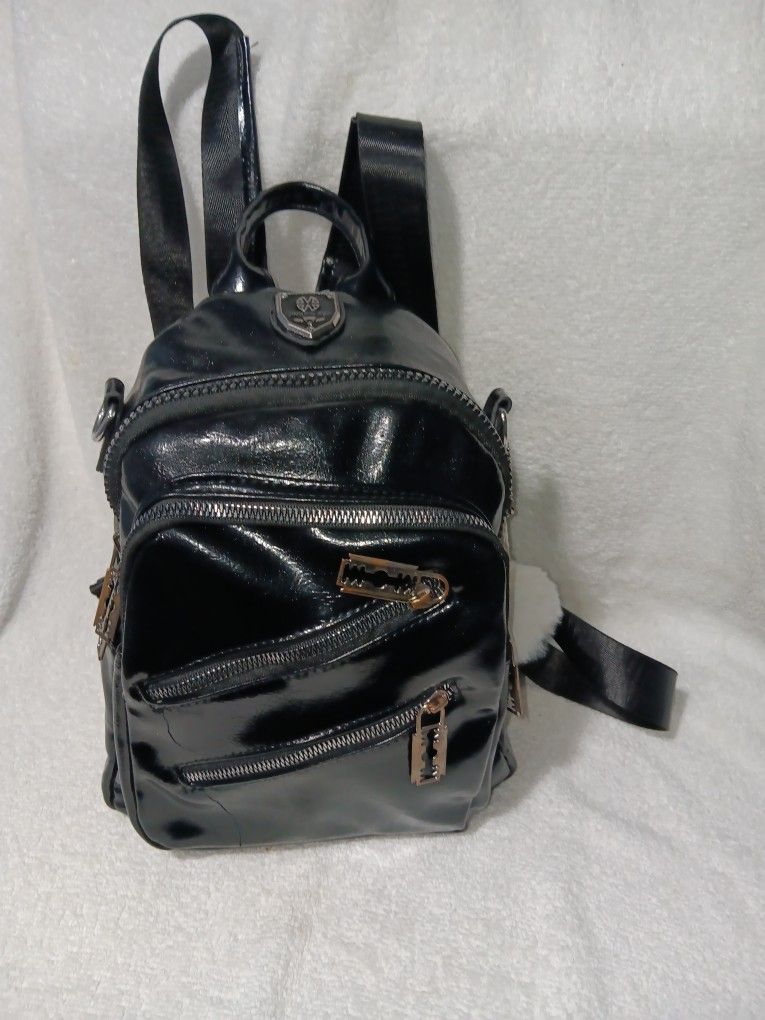 This is a small black patent faux leather backpack with multiple zipper pockets.