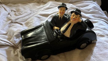 vintage ceramic or chalkware figurine depicting the iconic comedy duo Laurel and Hardy riding together in a black vintage car