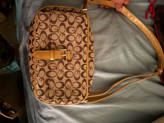 This vintage Coach Signature East West Shoulder Bag features a monogram canvas pattern with tan leather trim and a front buckle closure.