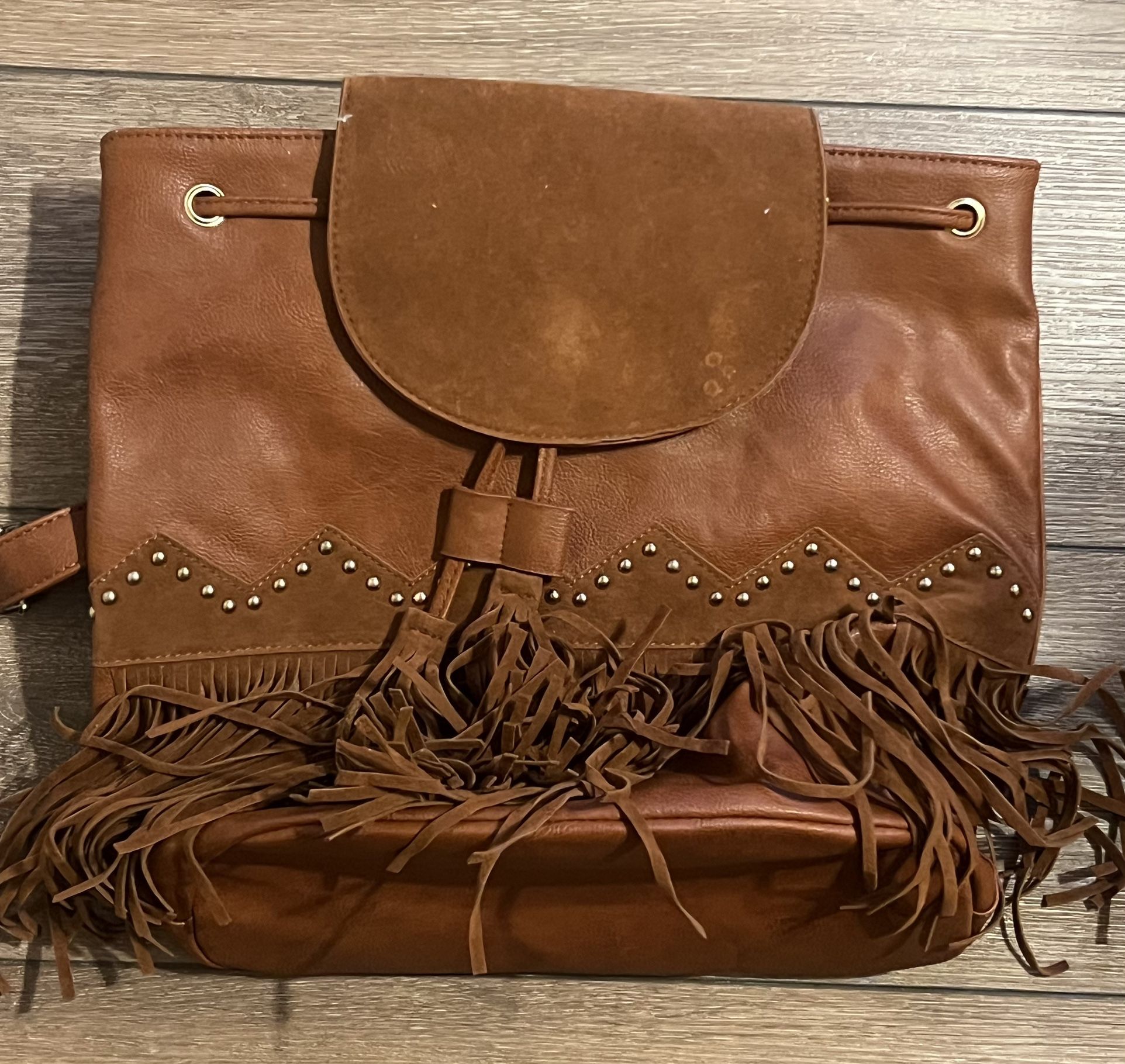 This is a brown faux leather backpack with fringe and stud details, similar to styles from American Eagle Outfitters and Classic Rock Couture