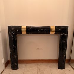 This is a Hollywood Regency style black marble fireplace mantel with brass detailing, in the manner of Karl Springer. 