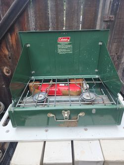 vintage Coleman 413H or 413G camp stove features a distinctive green steel case with a red fuel tank.