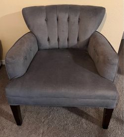 Tufted accent armchair with button-tufted backrest and arms, dark wooden legs, and gray upholstery fabric.