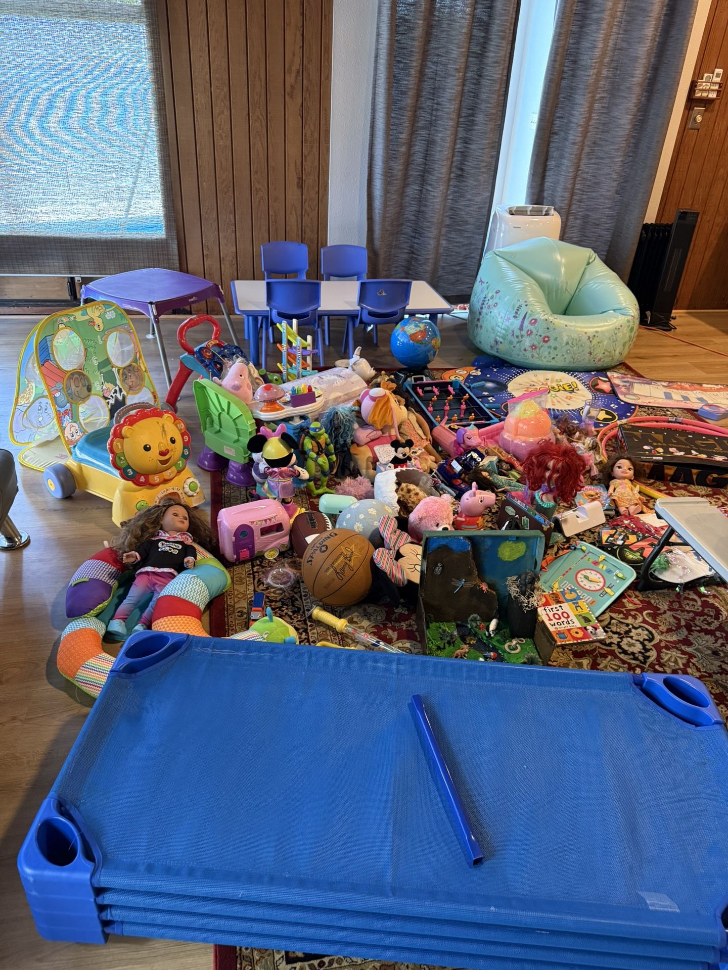 Four mattresses, a table with four chairs, a chair with a table, a colored chair, teddy bears, toys, boxes, a ball, toy animals, and a musical mat.