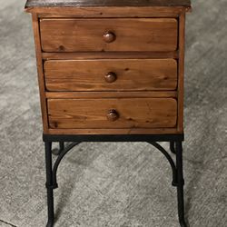 This is a three-drawer pine wood end table or nightstand with an industrial style metal base