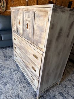 This vintage-style armoire features a whitewashed finish and distinct brass hardware pulls.