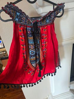 Lightweight bohemian off-shoulder top in vibrant red with decorative tribal print and black tassel accents. Elastic neckline for an easy, comfortable 