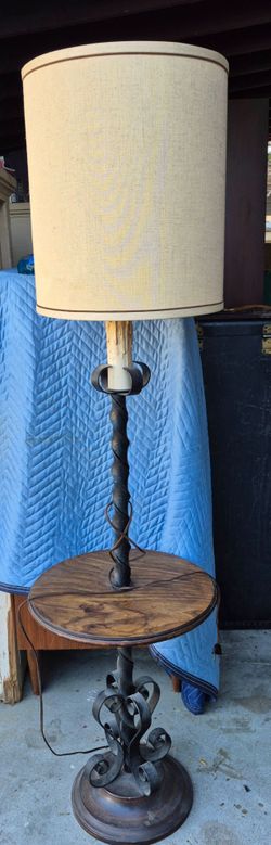 Presenting  a vintage  wrought-iron floor lamp with a twisted metal stem, an integrated round wooden tray table, a scrollwork base, and acylindrical f