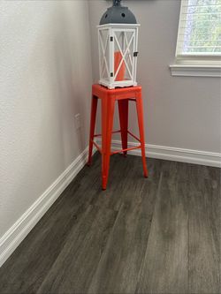Decorative white and gray lantern with orange candle and orange stool.