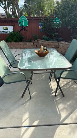 rectangular outdoor patio dining set with a glass-top table and matching green chairs