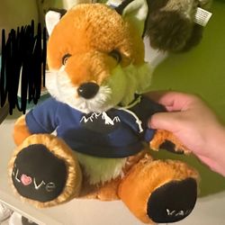 plush toy of a fox wearing a blue hoodie with a mountain design. Stuffed animal