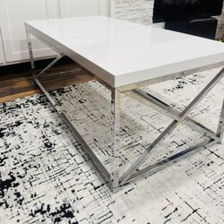 A modern contemporary coffee table with a glossy white top and a chrome metal base.
