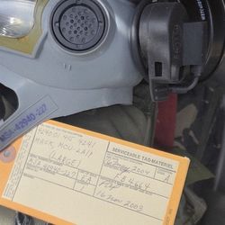 vintage military-issued chemical warfare protective mask, likely an MSA MCU-2A/P, along with its accompanying inspection tag. 
Item: A large-sized MSA