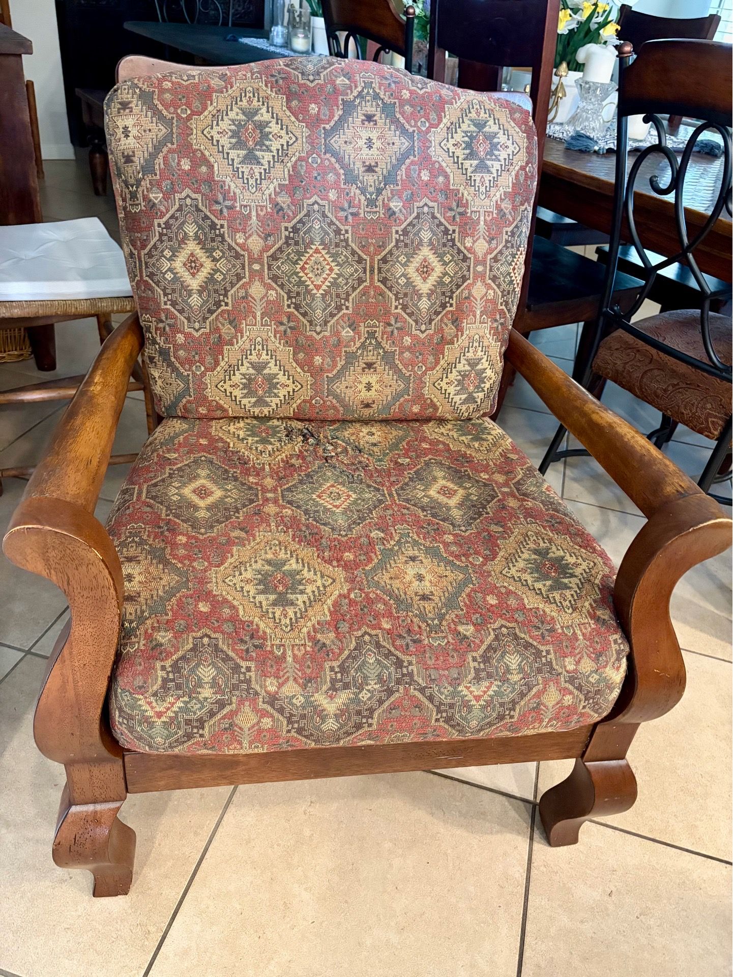 Sturdy wooden armchair has tapestry upholstery with red and gold geometric patterns. Frame is solid wood with curved armrests and decorative feet.