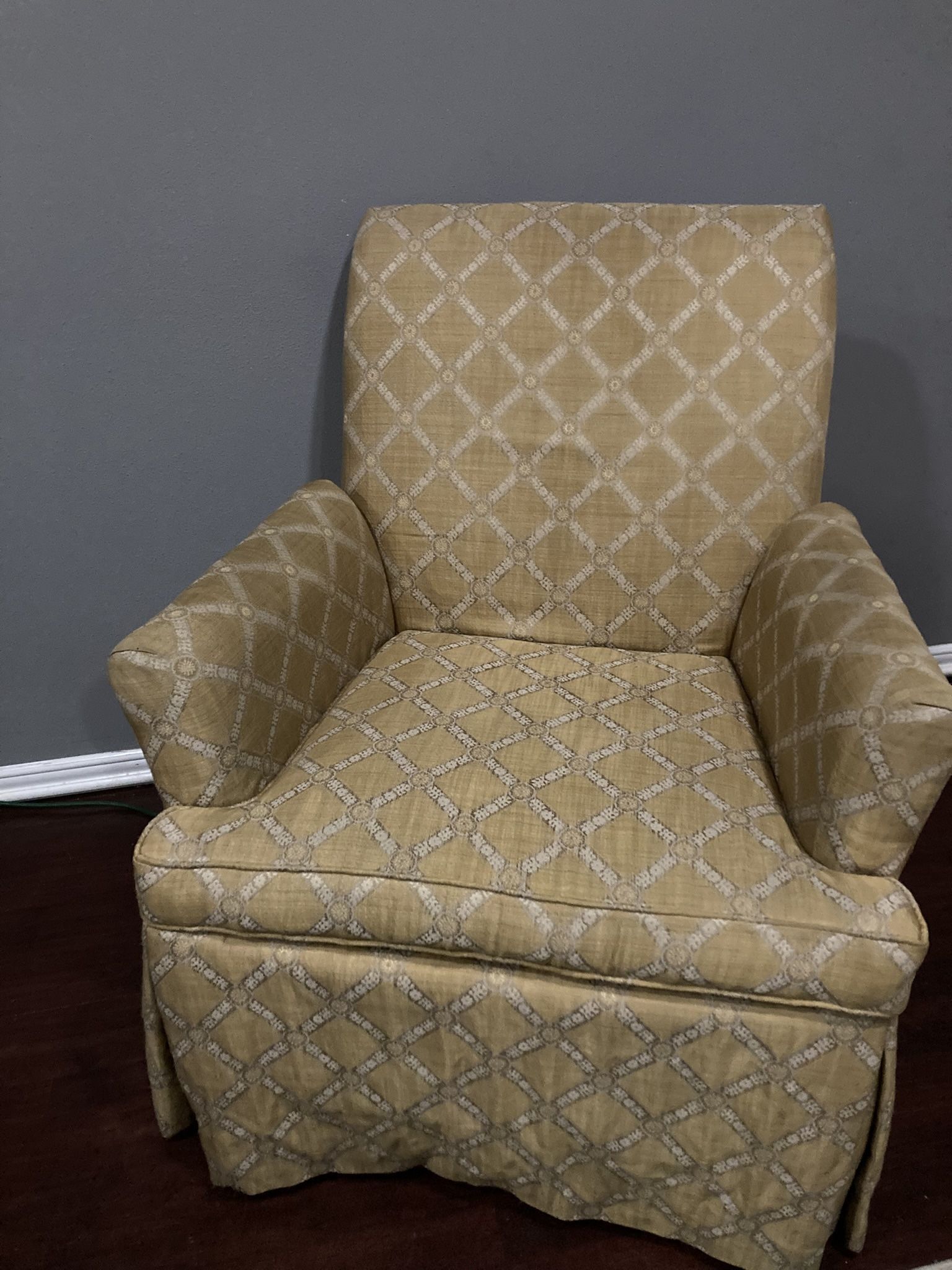 upholstered armchair with a rolled arm, low back, and a skirted base, featuring a gold and white geometric lattice pattern.