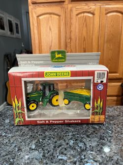 Ceramic John Deere Tractor Pulling A Wagon of Corn Pair Of Salt and Pepper Shakers.  Made in USA.  Brand new in box never removed.  The box is bent an