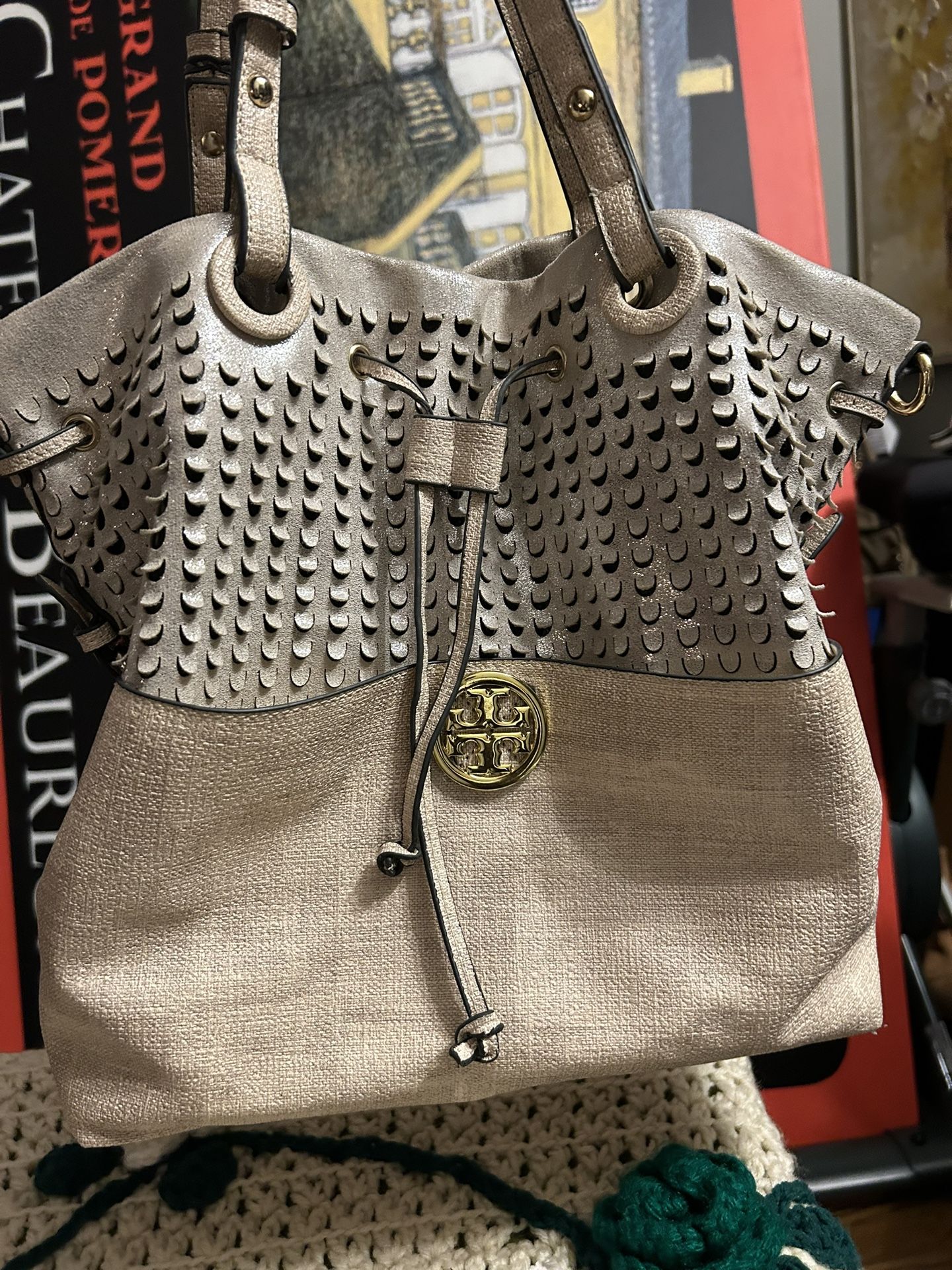 Fashion tote handbag. It's a light beige color with a gold logo and a drawstring closure.