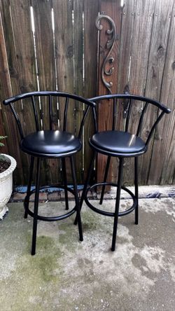 Sturdy metal bar stools in a sleek black finish. These stools have padded black vinyl swivel seats and a curved backrest design. Each stool has a buil