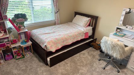 Brown wood twin bad frame with trundle and trundle mattress.