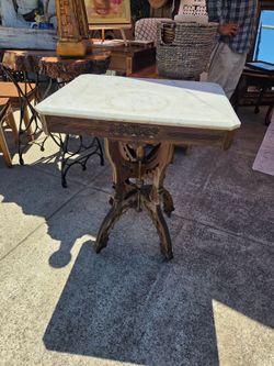 This antique Victorian Eastlake-style side table features an elegant white marble top and a carved wooden base with ornate curved supports.