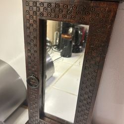 This is a hand-carved wooden vanity mirror or cabinet with a dark finish and a latching door. 