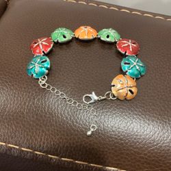  is a multicolored sand dollar link bracelet with an adjustable chain. 