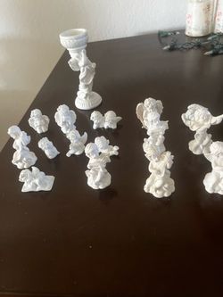 Elegant collection of white resin angel and cherub figurines. This set includes thirteen small cherub figures in various poses and one taller angel-th