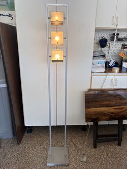 This is a modern metal floor lamp featuring a tall rectangular frame and three stacked, square frosted glass light fixtures.