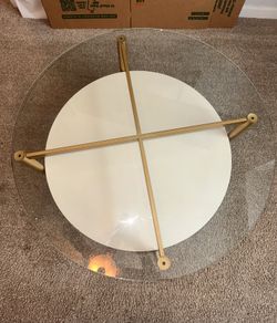 Round glass coffee table with gold frame and white shelf