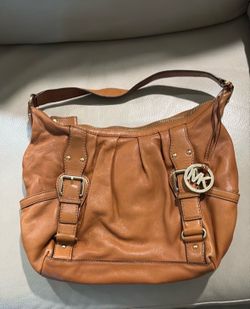 Leather MK hand bag with gold tone buckles, studs and a hanging round MK logo charm.