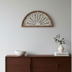Beautiful arched wall decoration with a rustic wood frame and a decorative white sunburst design. It features natural-looking beads for a charming, fa